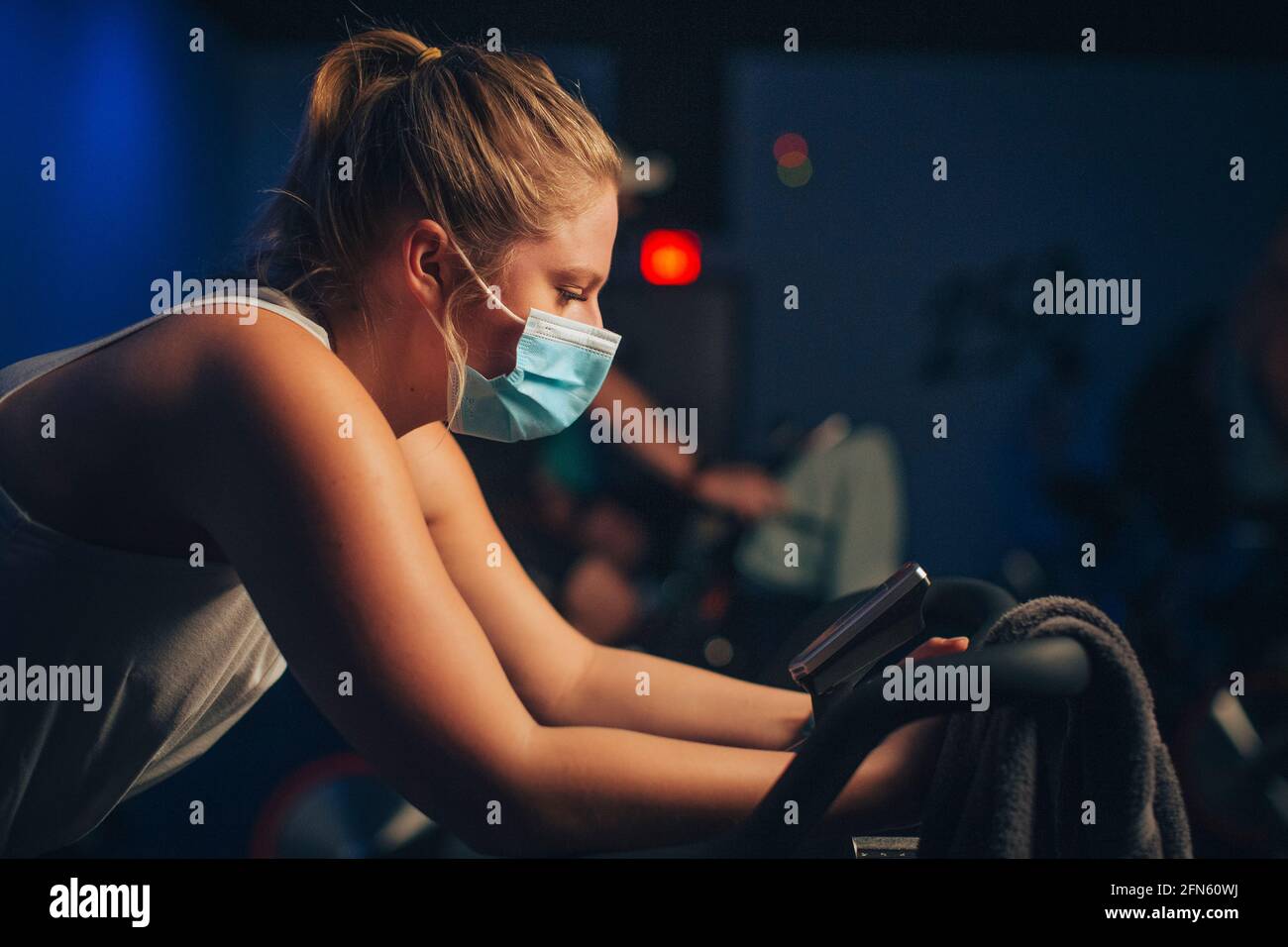Une femme caucasienne pédales dans un studio de cyclisme d'intérieur avec un masque. Banque D'Images