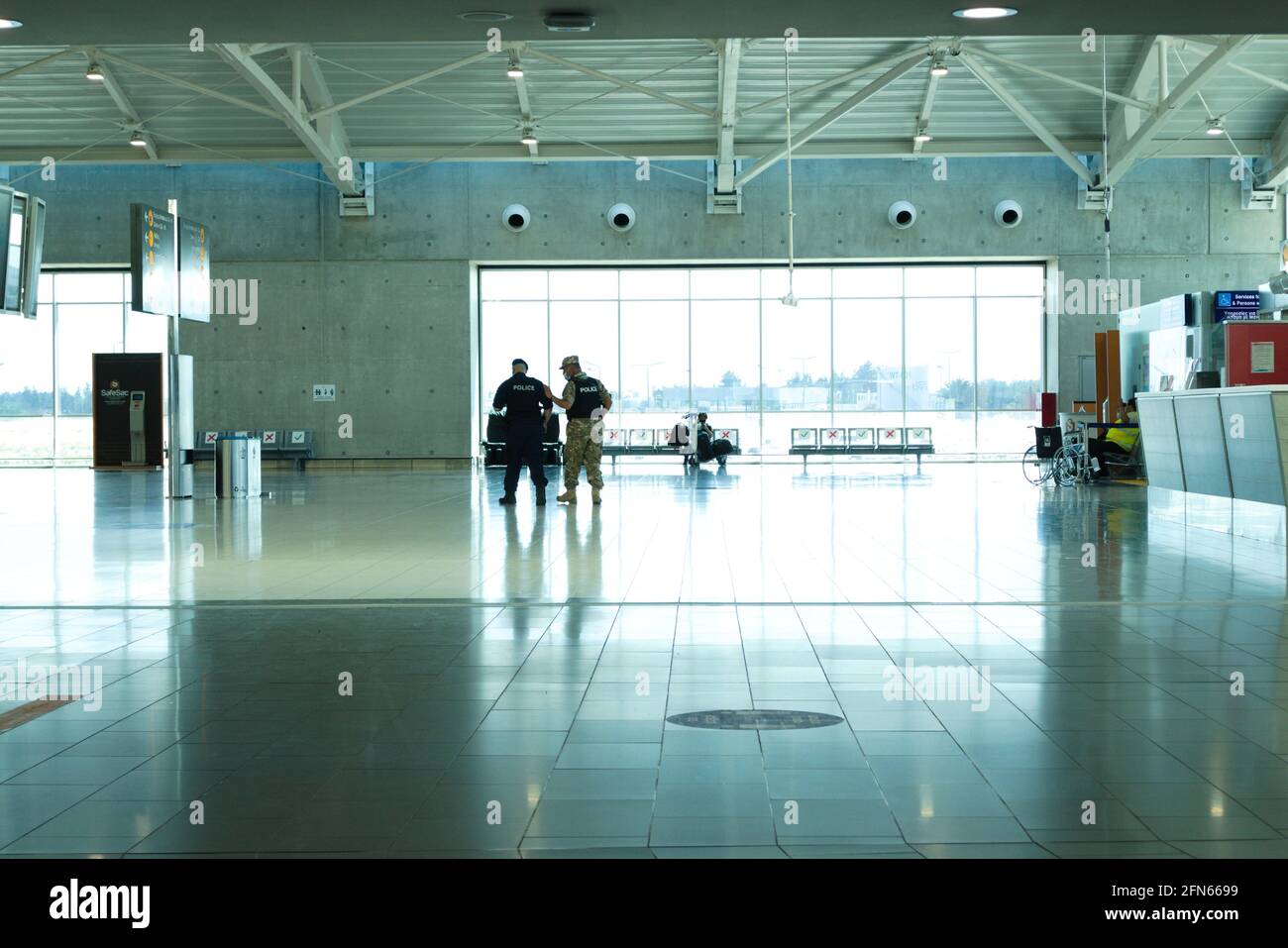 Larnaca – Chypre – 12 mai 2021 : deux policiers et une seule femme voyageant dans le terminal de départ vide de l'aéroport de Larnaca Banque D'Images