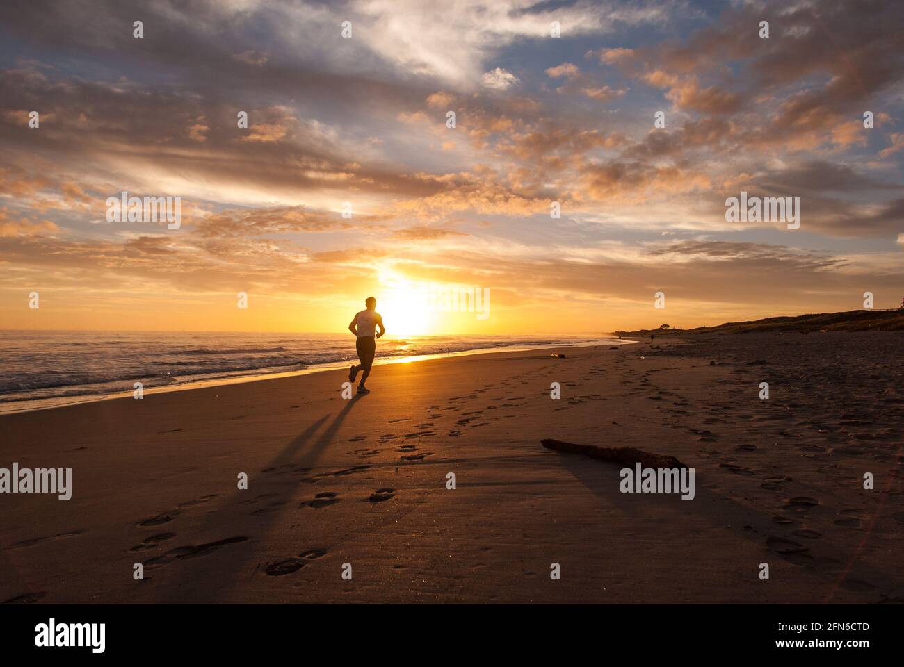 La course au sommet : un merveilleux début de journée avec un coureur solitaire au lever du soleil à Papamoa Beach, en Nouvelle-Zélande. Banque D'Images