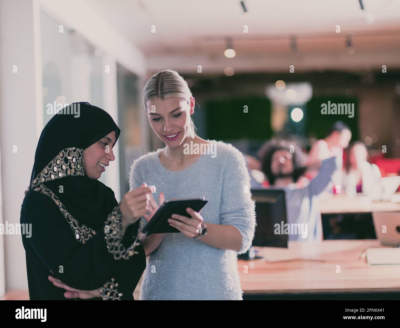 Blonde et moderne femme d'affaires musulmane amis collaborant en équipe et travaillant sur tablette. Une équipe diversifiée dans un bureau à espace ouvert moderne en arrière-plan Banque D'Images