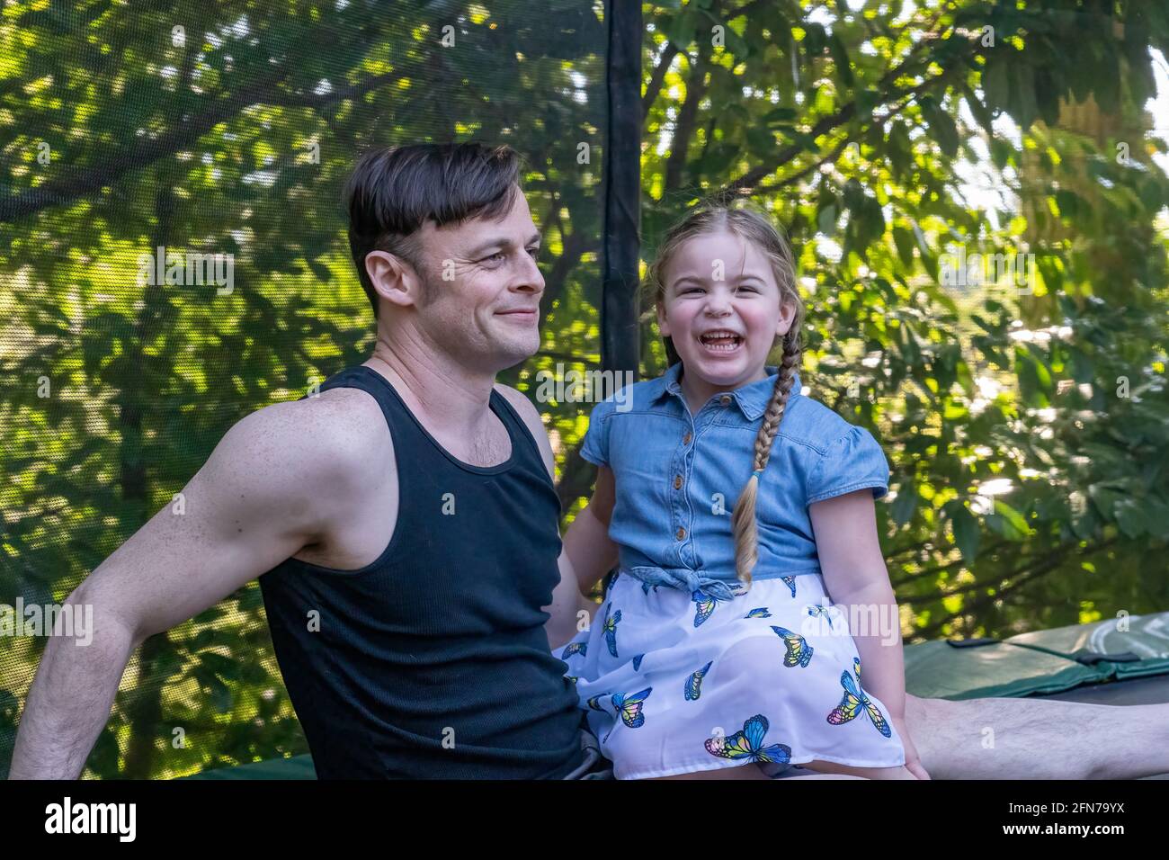 Lynwood, Washington, États-Unis. Père et fille de quatre ans prenant un repos sur leur trampoline arrière-cour après le jeu. Banque D'Images