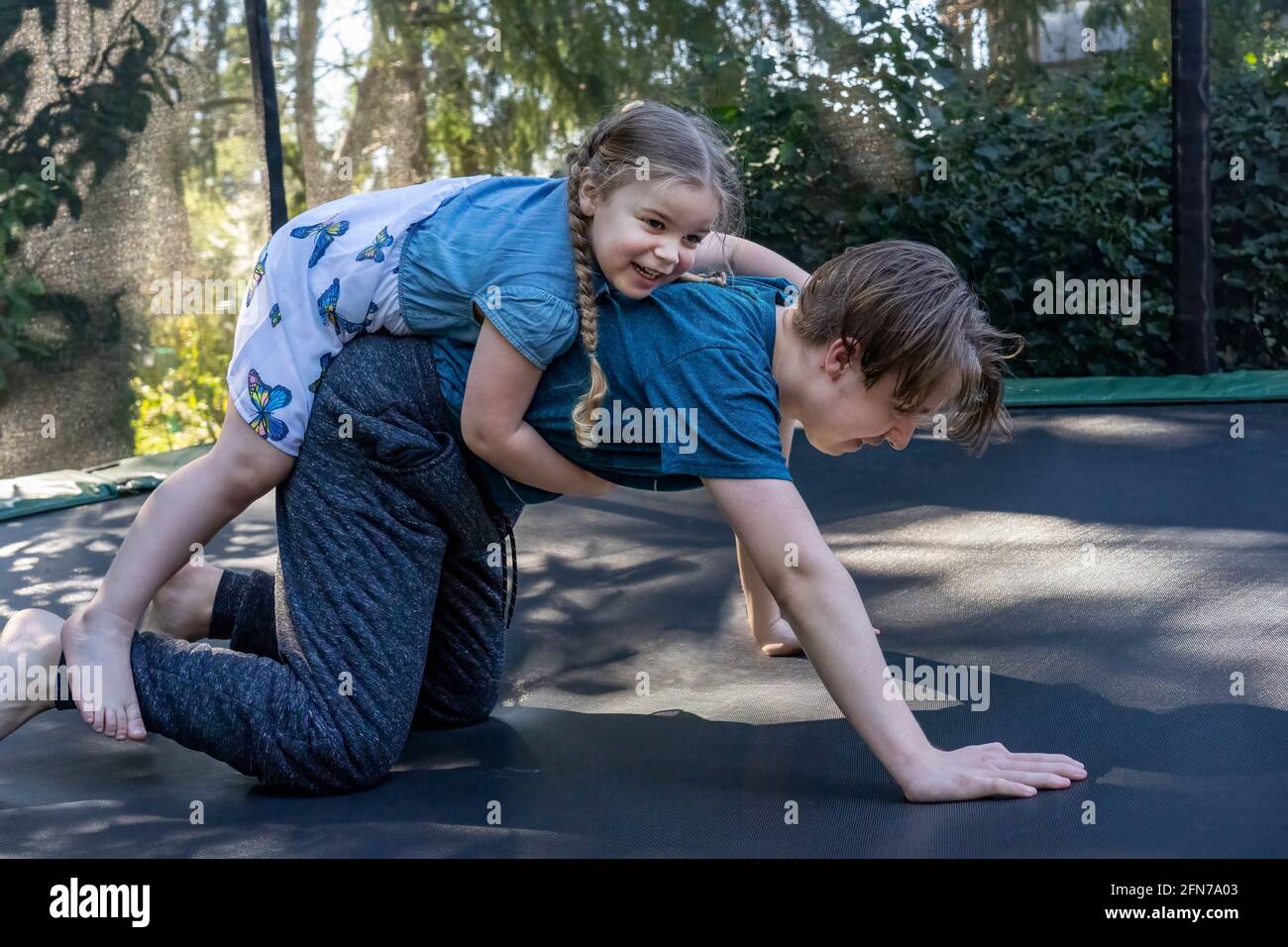 Lynwood, Washington, États-Unis. Fille de quatre ans essayant de grimper sur le dos de son frère adolescent sur le trampoline. (M.) Banque D'Images