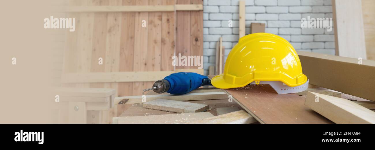 Le casque de construction jaune et la perceuse électrique bleue ont été laissés de côté pendant le frein de temps de déjeuner. Un bureau rempli d'outils à main et de piles de bois. Matin Banque D'Images