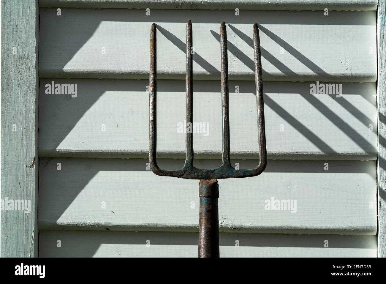 Fourche de jardin projetant des ombres sur des panneaux d'intempéries éclairés par le soleil Banque D'Images