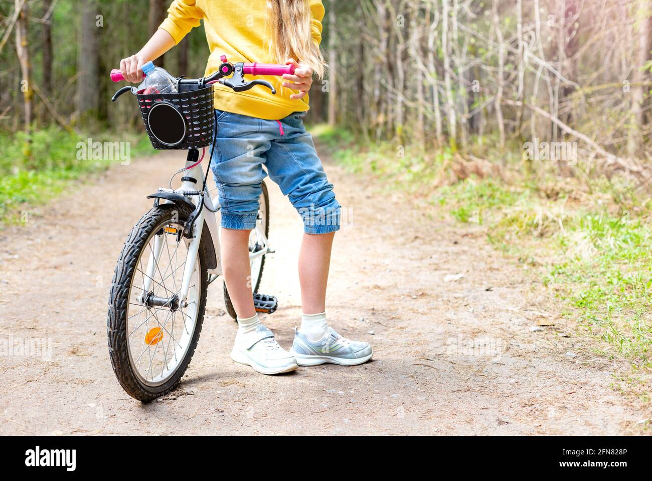 Une fille est debout avec un vélo sur un chemin dans un parc ou une forêt par un jour ensoleillé d'été. Banque D'Images