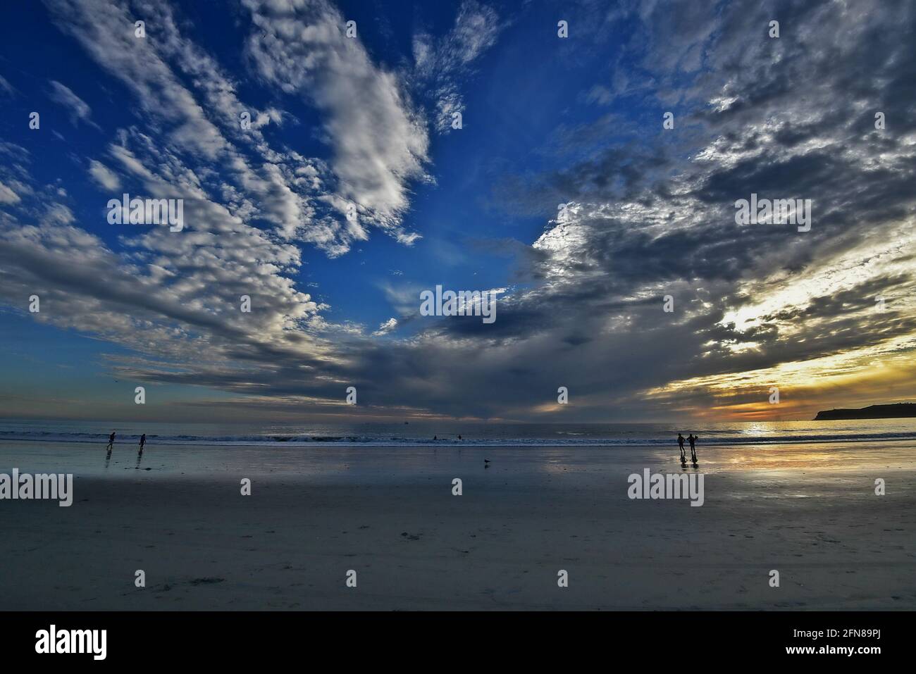 Coucher de soleil avec vue panoramique sur la plage de Coronado Island et les silhouettes de personnes marchant sur le sable humide, dans le sud de la Californie de San Diego. Banque D'Images