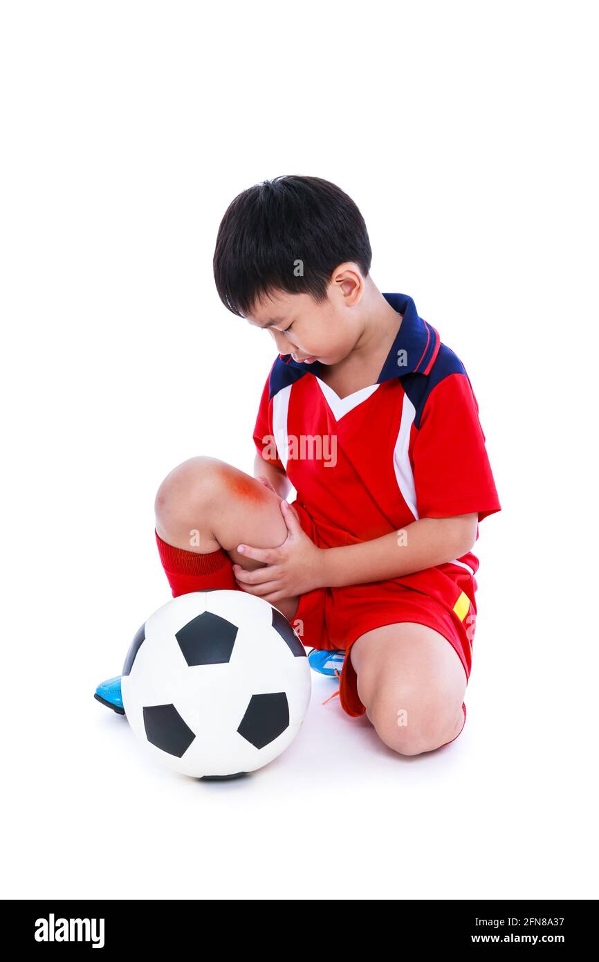 Blessures sportives. Jeune joueur asiatique de football avec un ballon de football en uniforme rouge blessé à la jambe. Isolé sur fond blanc. Prise de vue en studio. Corps entier. Banque D'Images