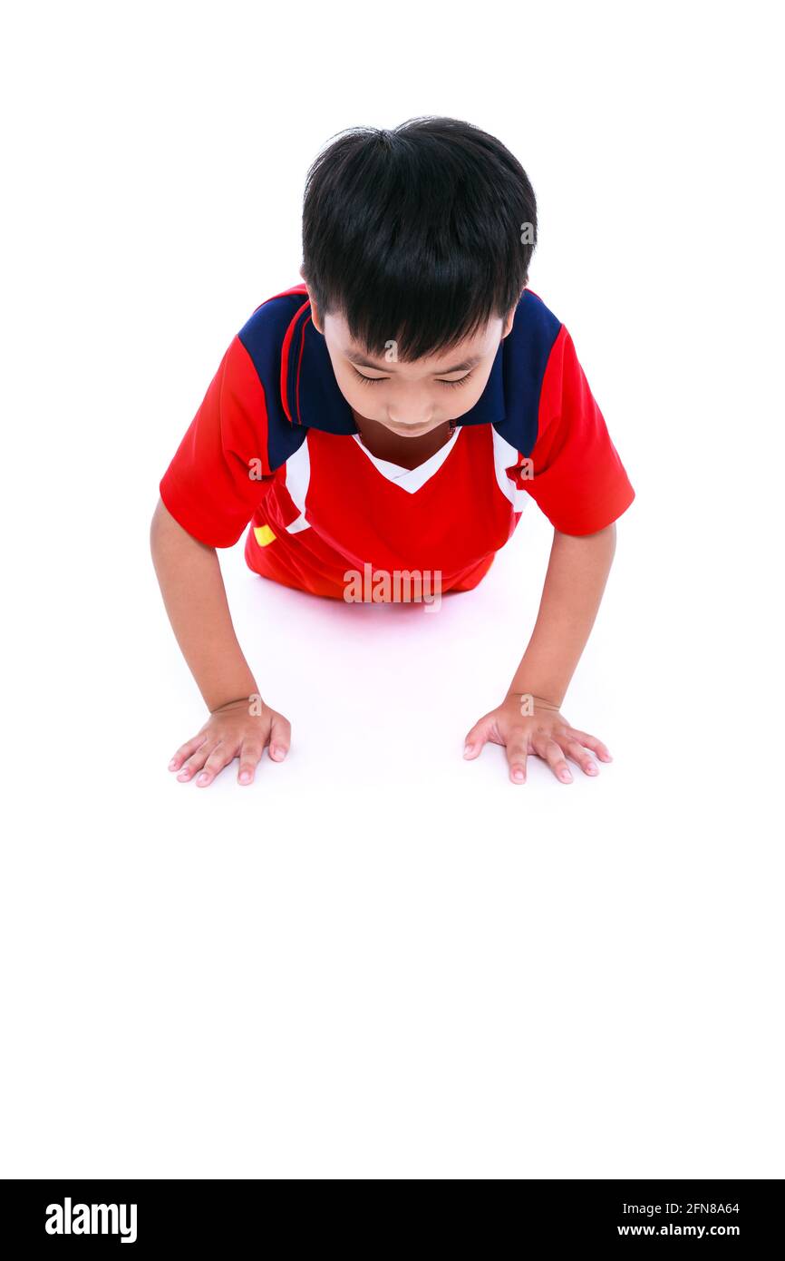 Exercices de poussée ou de pression par un jeune joueur asiatique de football en uniforme rouge. Entraînement d'enfant athlète, tir en studio. Isolé sur fond blanc. Spor Banque D'Images