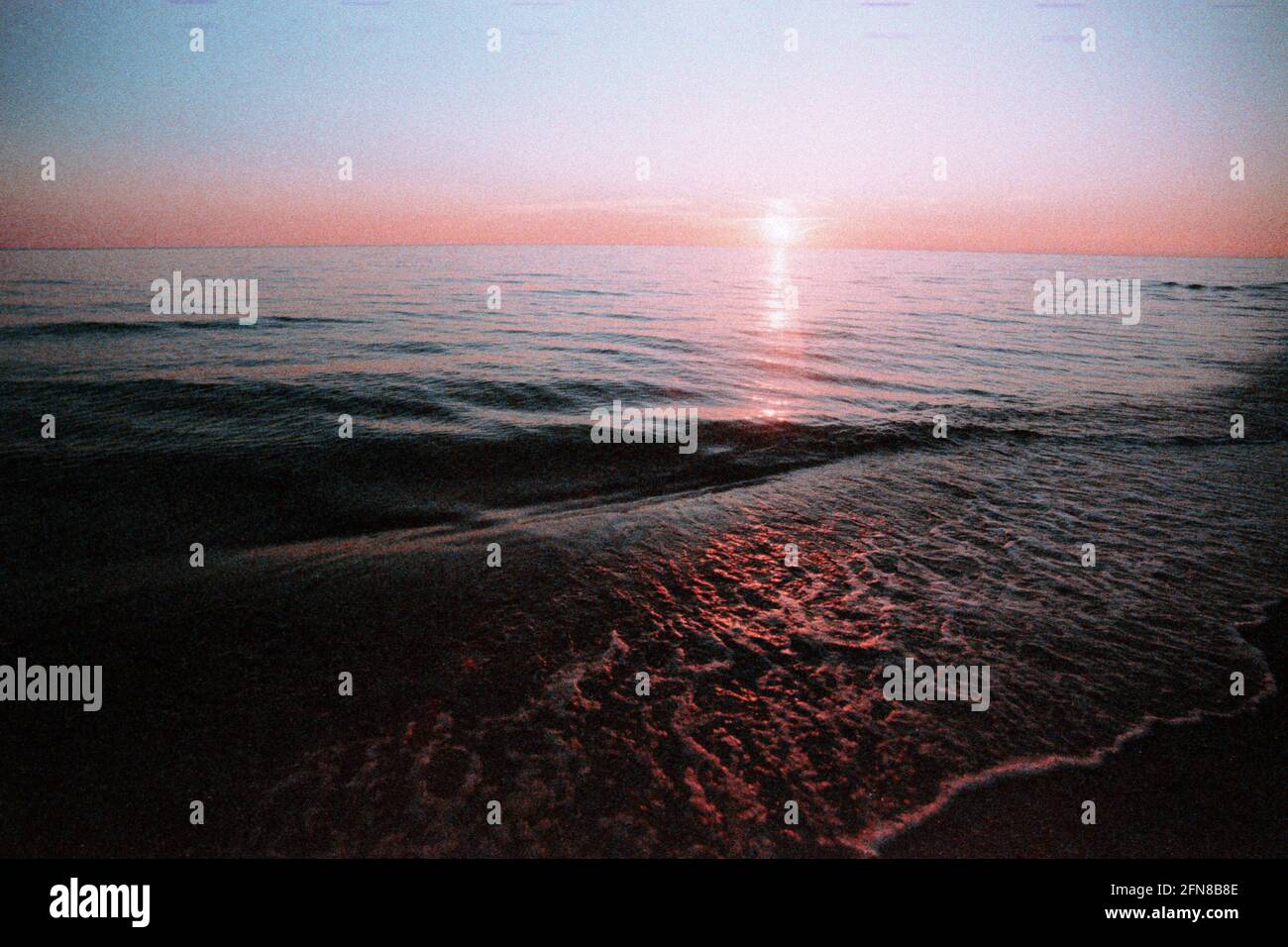Coucher de soleil sur la mer Baltique, le film a des grains. Coucher de soleil rouge sur le bord de la mer. Fond marin dans un style vintage. Soleil, ciel, des vagues et du sable. Banque D'Images