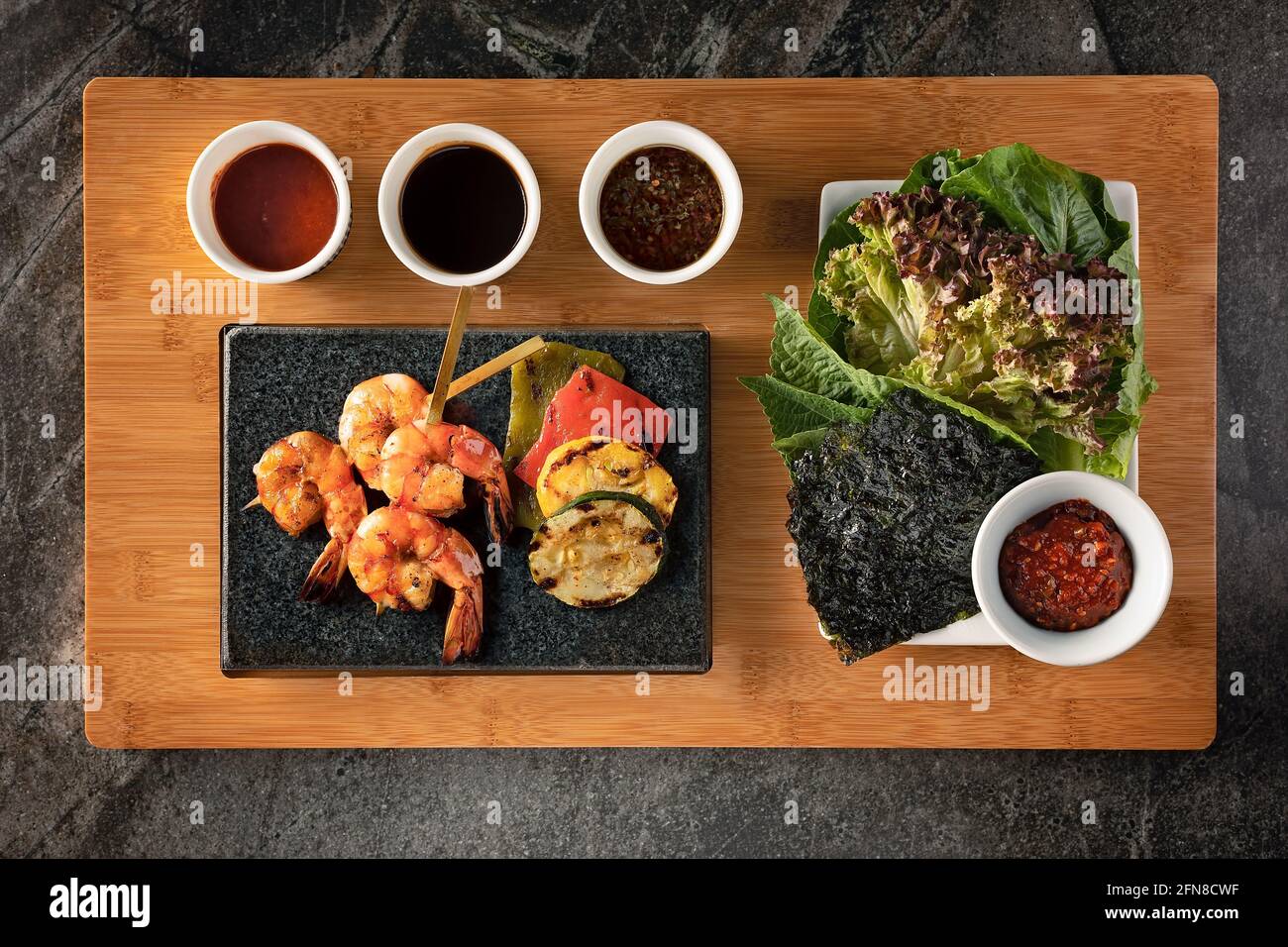 Plat d'un barbecue coréen avec crevettes grillées, légumes, salade et sauces Banque D'Images