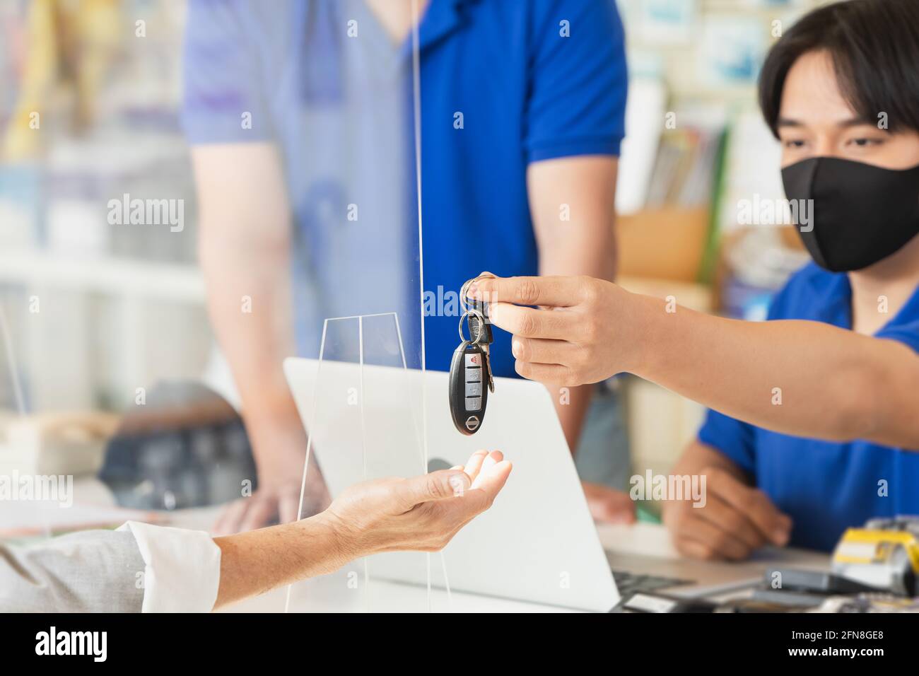 le personnel de la réception donne la clé de voiture au client. Jeune homme travaillant dans un centre de service de voiture de garage portant un masque facial pour les soins de santé. Banque D'Images le personnel de la réception donne la clé de voiture au client. Jeune homme travaillant dans un centre de service de voiture de garage portant un masque facial pour les soins de santé. Banque D'Images