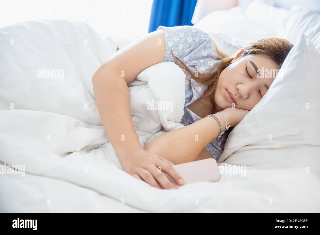Les femmes dormant dans un lit blanc confortable, asiatique chubby jeune fille de graisse de repos avec le téléphone cellulaire. Banque D'Images