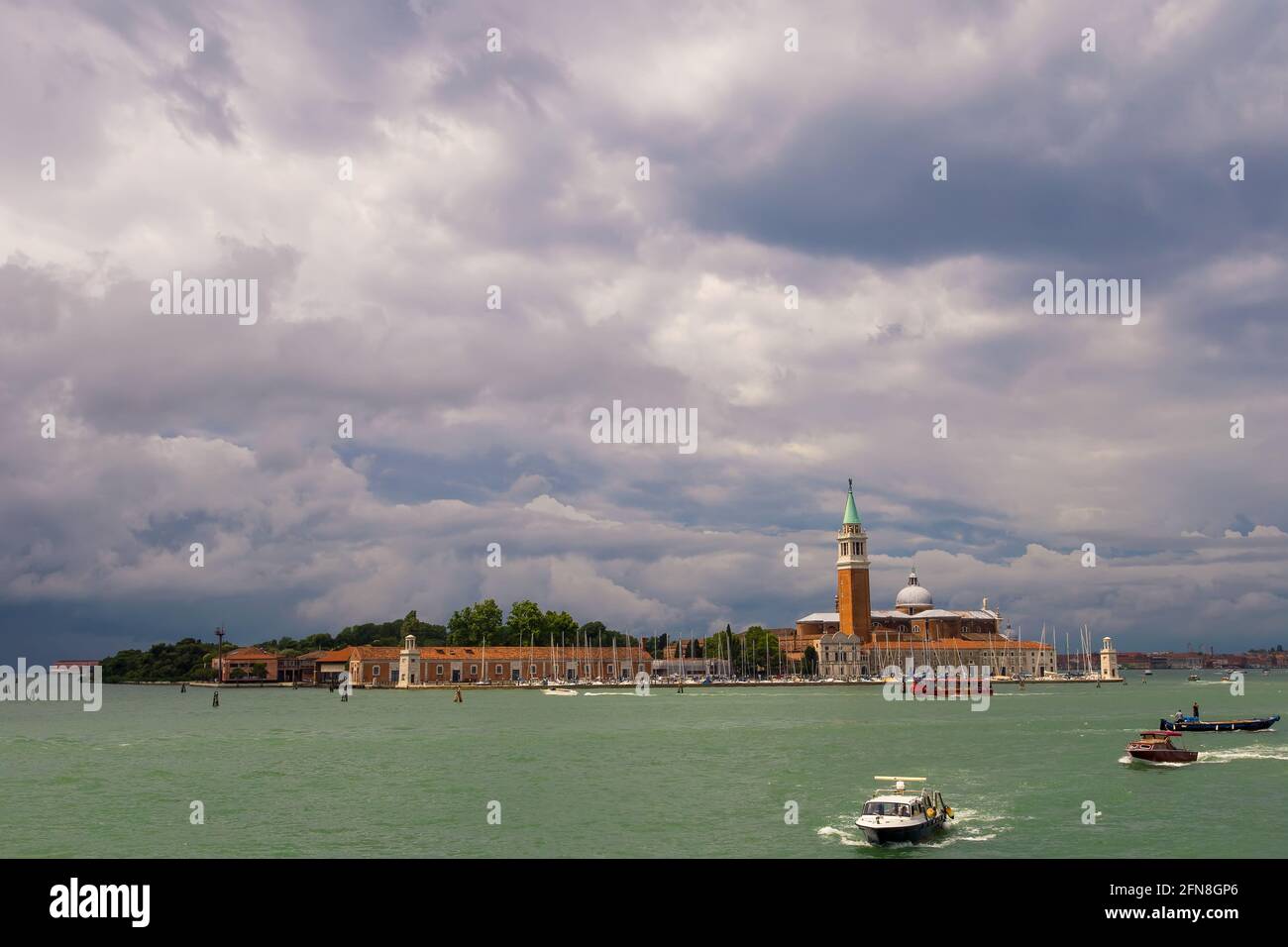 Basilique de San Giorgio Maggiore au coucher du soleil. Des bateaux naviguent le long du canal. Soirée d'été, nuages sombres dans le ciel. Italie, Venise. Banque D'Images
