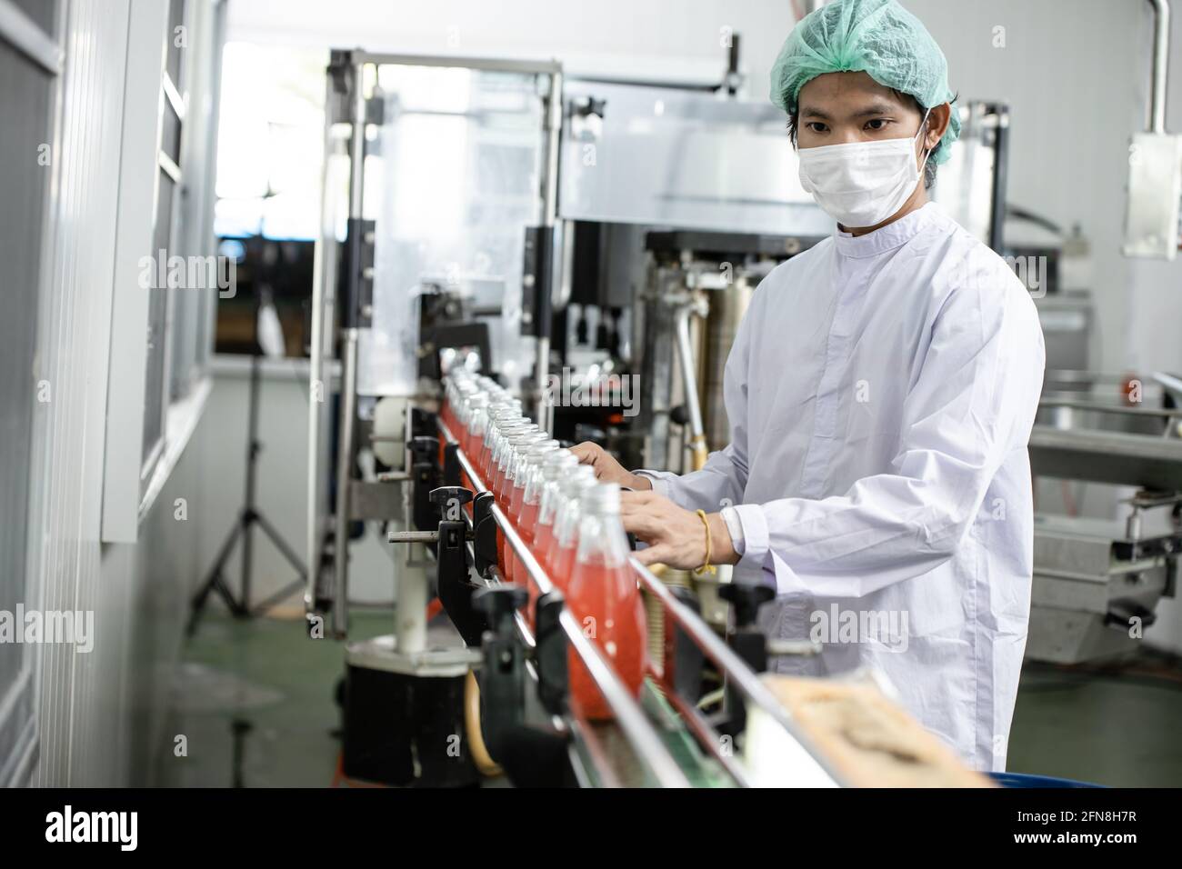 Travailleur de l'hygiène travaillant dans une usine de boissons sur un tapis roulant avec du verre de jus de fruits en bouteille dans la chaîne de production. Banque D'Images