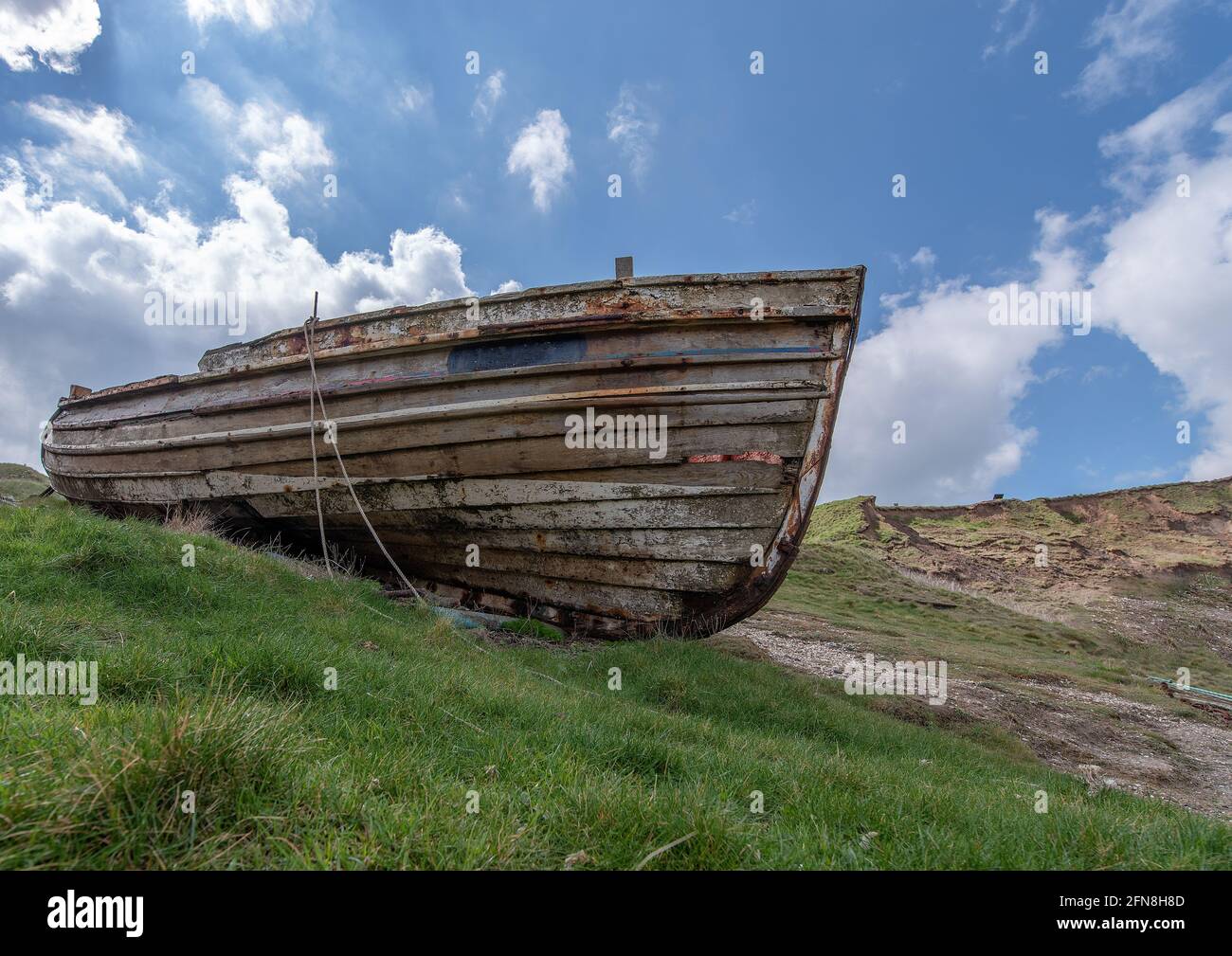 Un bateau de pêche en bois éloigné a été pêché sur un talus d'herbe le jour ensoleillé avec fond bleu ciel. Banque D'Images