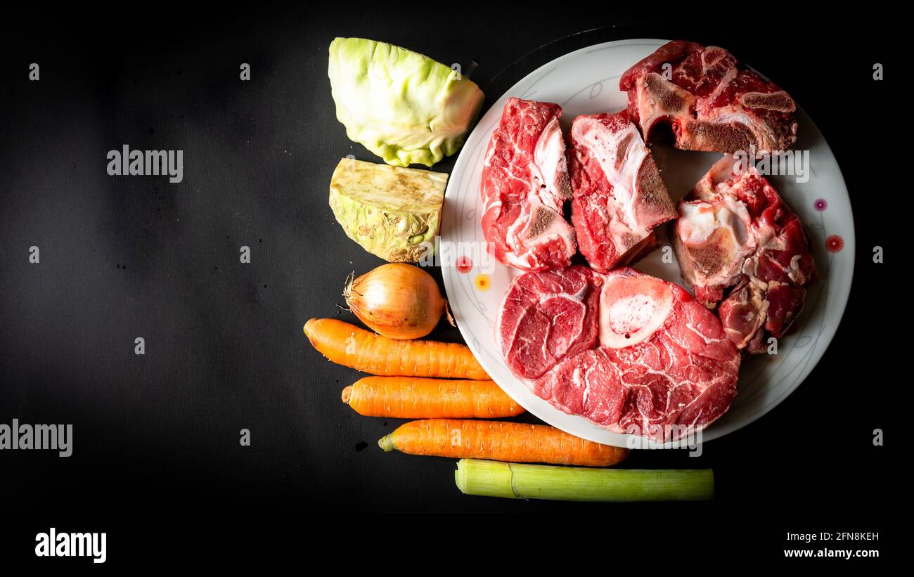 Nourriture non cuite. Les os de bœuf crus et les légumes sur fond noir