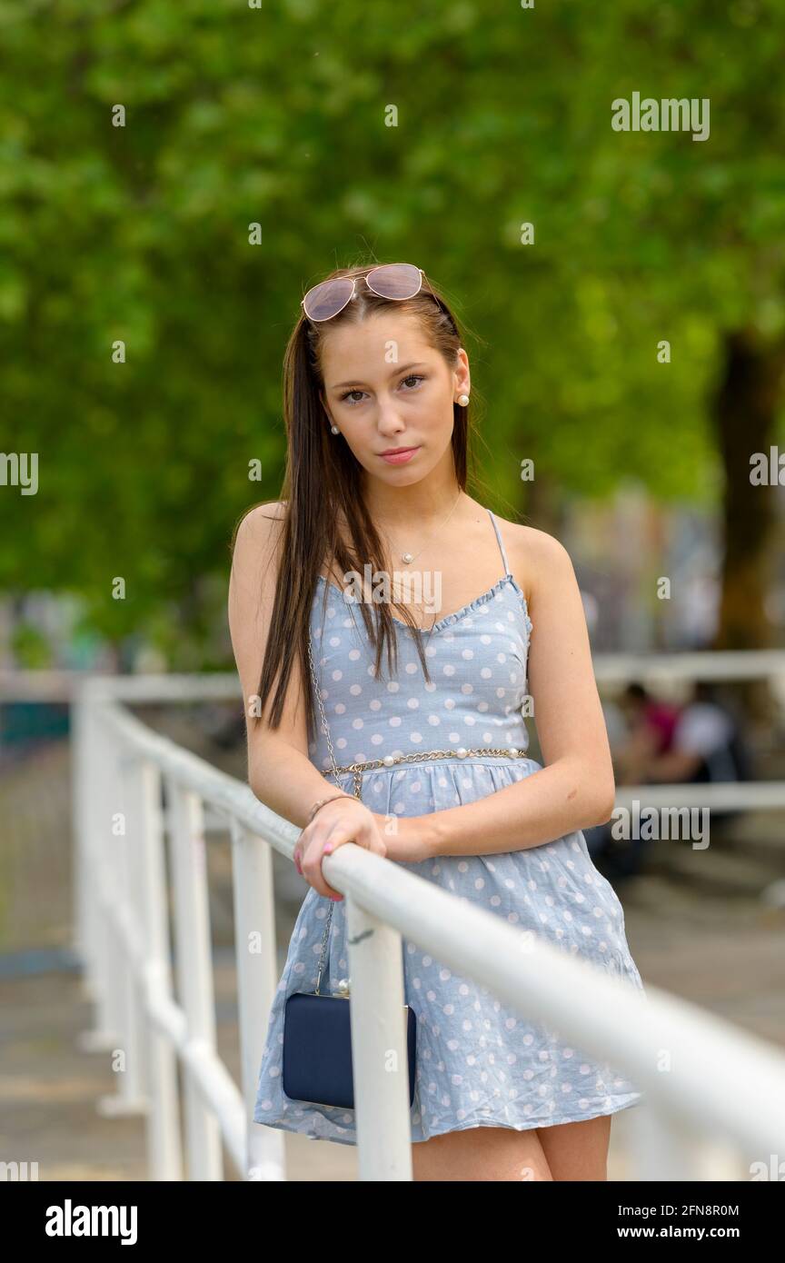 Portrait d'une jolie jeune femme, prise en été dans une ville, penchée contre une rampe sur une rivière voisine. Banque D'Images