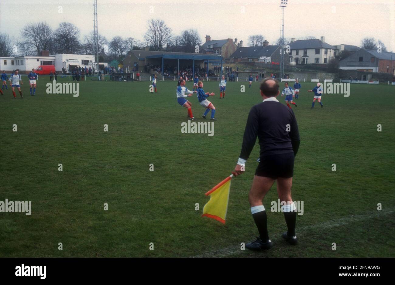 Un joueur de ligne avec un drapeau jaune regarde le match sur un terrain de football non-League Banque D'Images