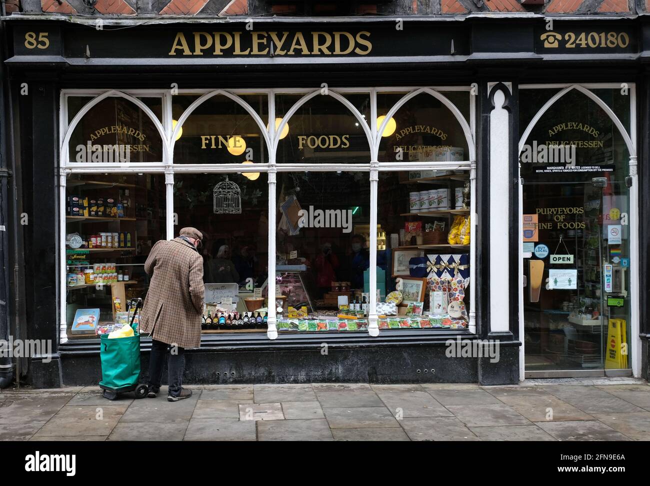 Un vieil homme en pardessus et en tissu de fenêtre de chapeau shopping à Appleyards traditionnel delicatessen sur Wyle COP, Shrewsbury, Shropshire, Angleterre Banque D'Images