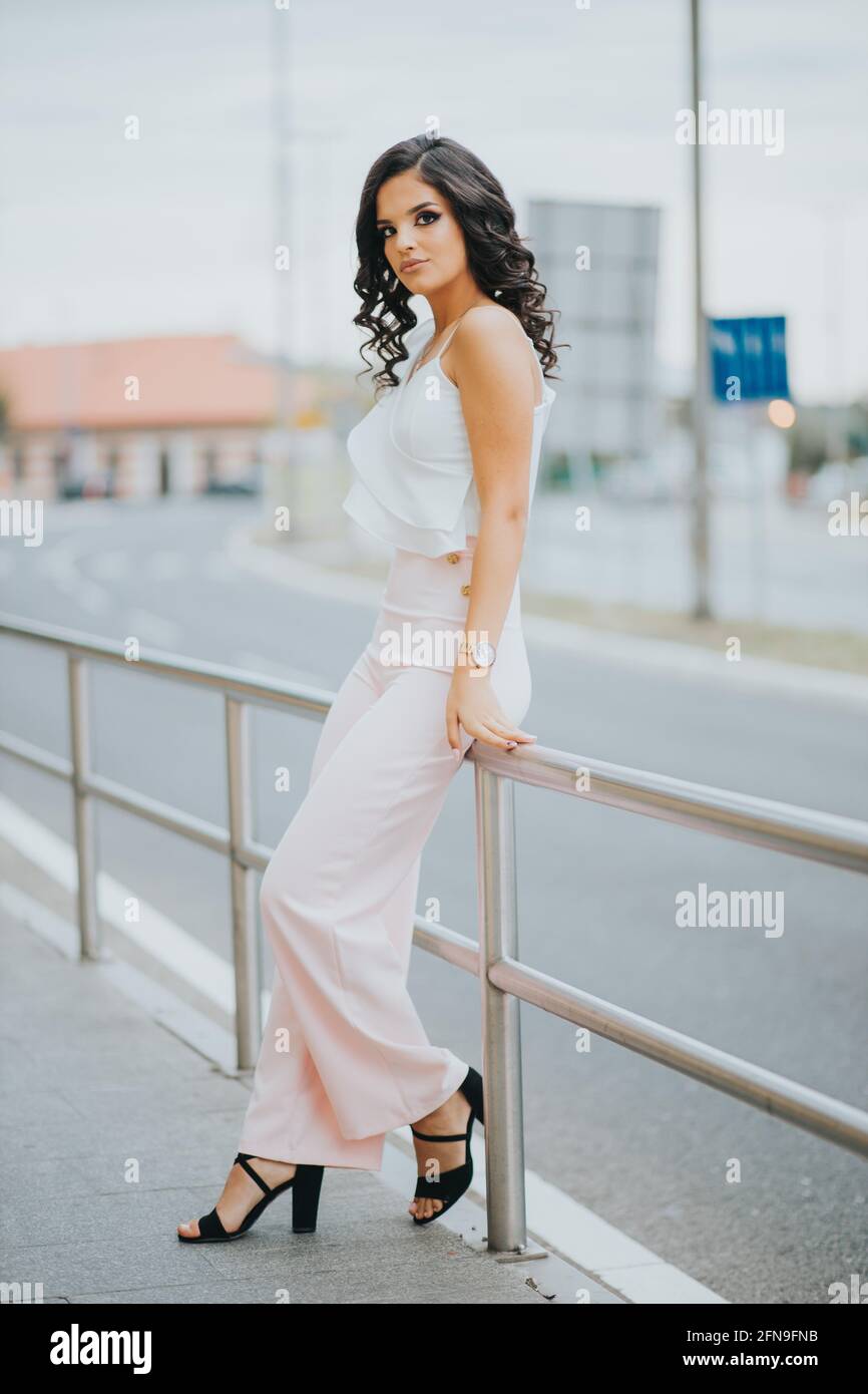 Sublime femme dans une élégante tenue rose et blanche sur une clôture  urbaine Photo Stock - Alamy