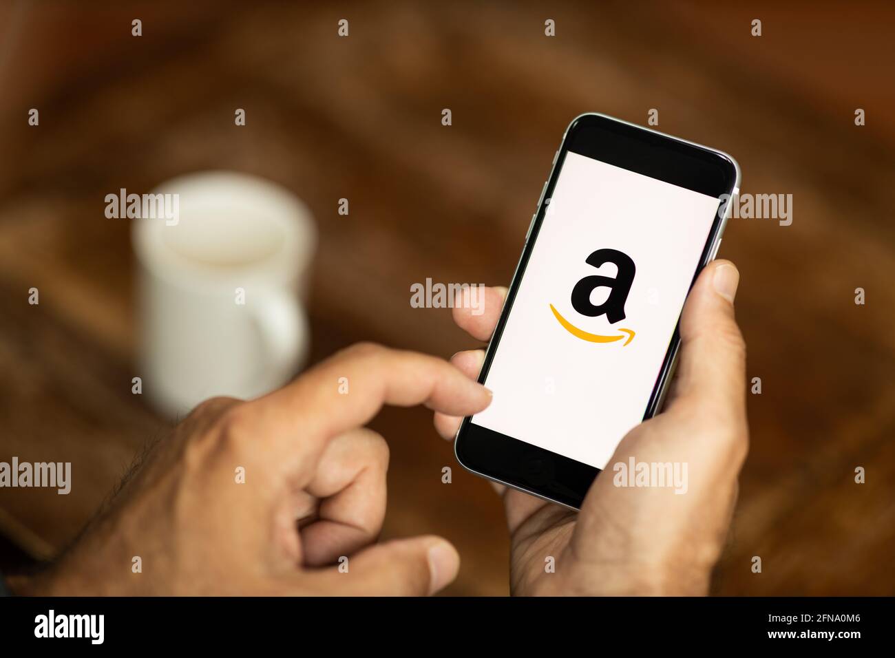 Homme tenant un smartphone dans un café. Logo Amazon sur l'écran. Mise au point sélective. Banque D'Images