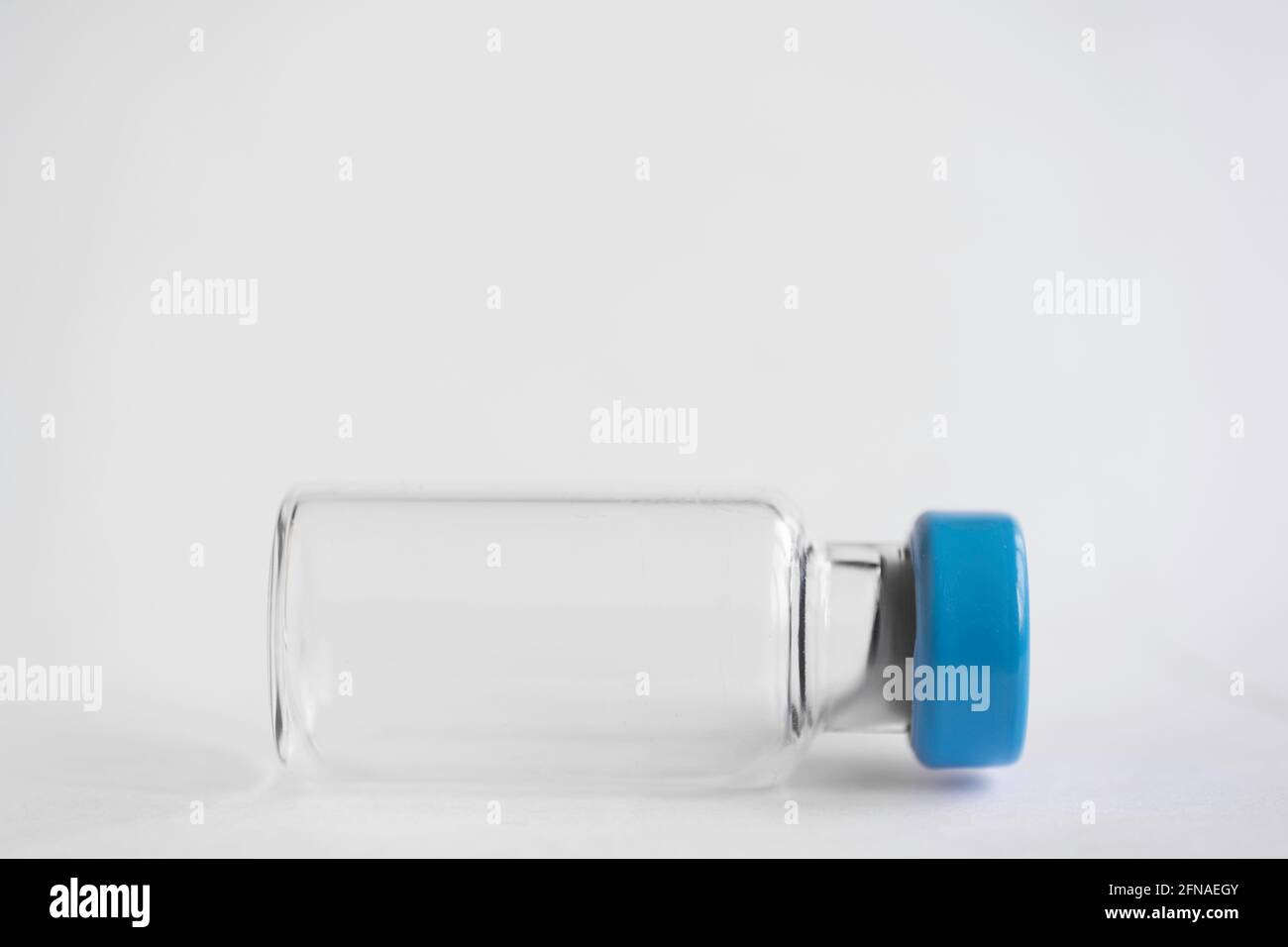 Flacon de vaccin en verre corona avec bouchon bleu sur fond blanc. Faible profondeur de champ. Copier l'espace Banque D'Images