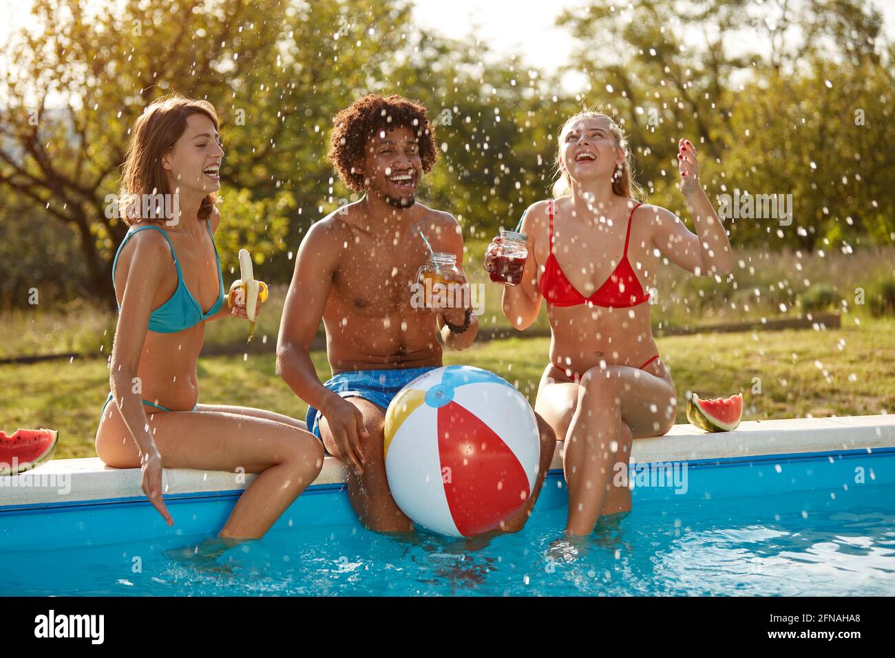 jeune homme afro-américain s'amusant avec deux femmes caucasiennes en plein air dans la nature au bord de la piscine Banque D'Images