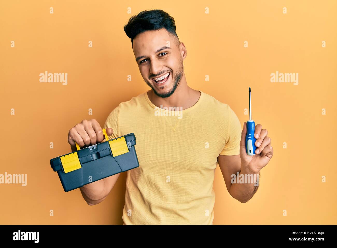 Un jeune homme arabe tient sa boîte à outils et son tournevis souriant et  riant fort parce que drôle de blague folle Photo Stock - Alamy