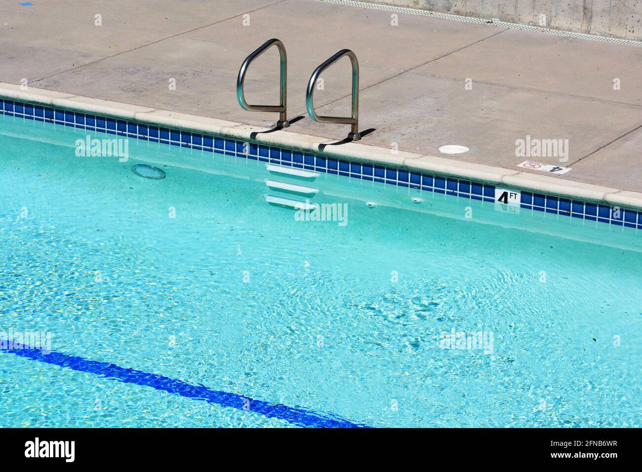 Vue en hauteur de la piscine extérieure avec mains courantes en métal avec marches, marqueur de profondeur sur le bord de la piscine, éclairage sous-marin et ligne bleue sur t Banque D'Images