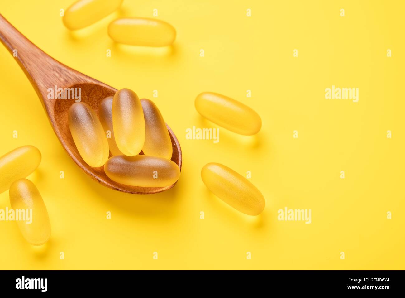 Cuillère en bois avec pilules Omega 3 sur fond jaune. Compléments alimentaires en capsules de vitamine D. Vue de dessus. Espace de copie - image Banque D'Images