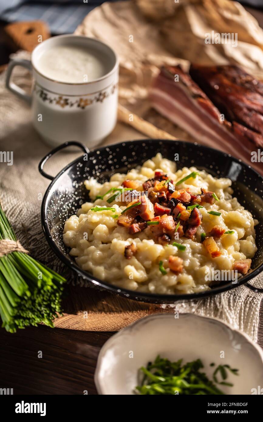 Brushky Bryndzove, la nourriture nationale de Slovaquie, servie avec du bacon, de la ciboulette et une tasse de lait aigre. Banque D'Images