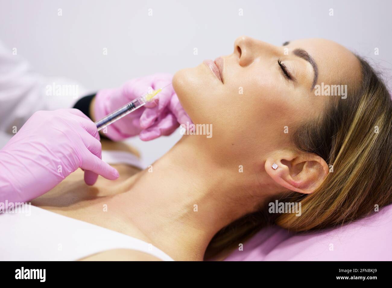 Médecin injectant de l'acide hyaluronique dans le ching d'une femme comme traitement de rajeunissement facial. Banque D'Images