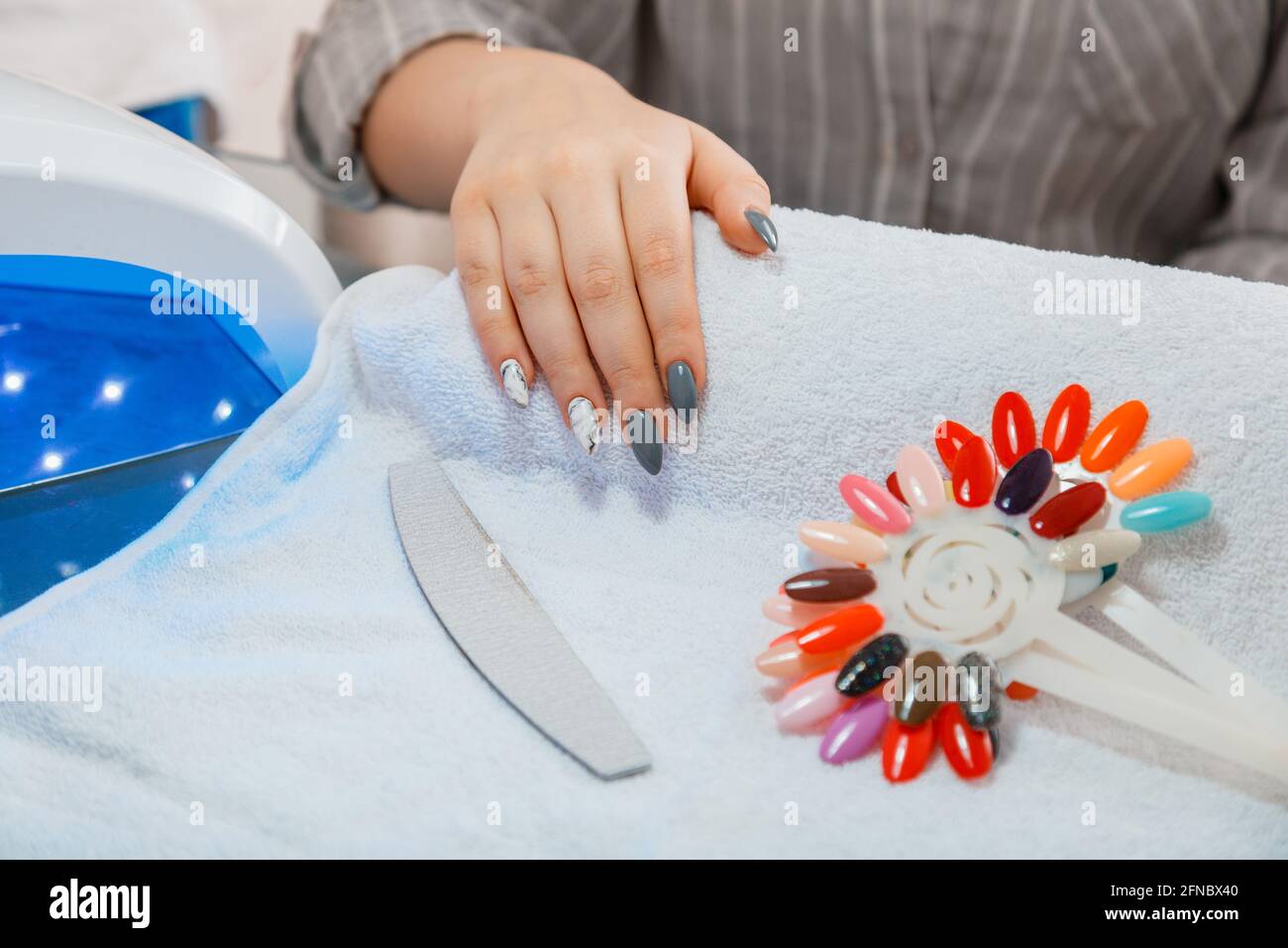 Femme avec des ongles acryliques artificiels ramasse une nouvelle couleur de polissage lors de la procédure de manucure. Traitement de manucure dans le salon de beauté sur une serviette blanche. Hygiène Banque D'Images