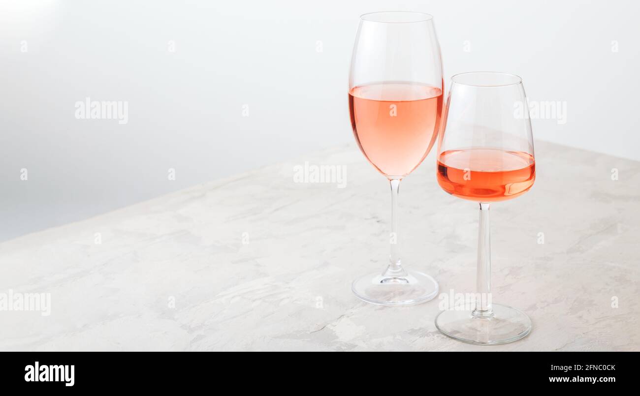 Vin de rose dans différents types de verres sur fond de béton léger. Composition minimale de vin sur table blanche. Longue bannière Web avec espace de copie. Banque D'Images