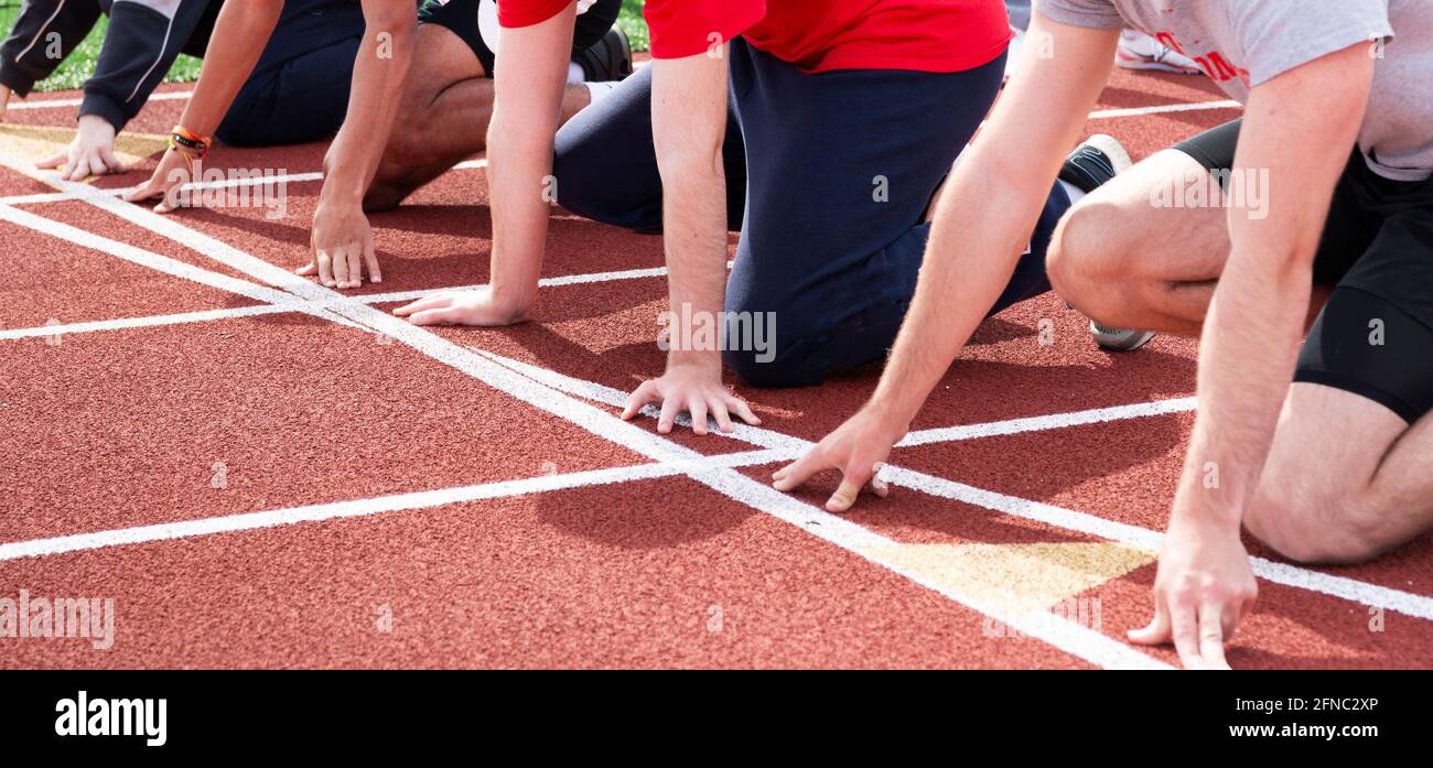 Les garçons du secondaire suivent des courses et des coureurs sur le terrain à la ligne de départ, prêts à démarrer une course de sprint sur une piste rouge sur piste et sur le terrain. Banque D'Images