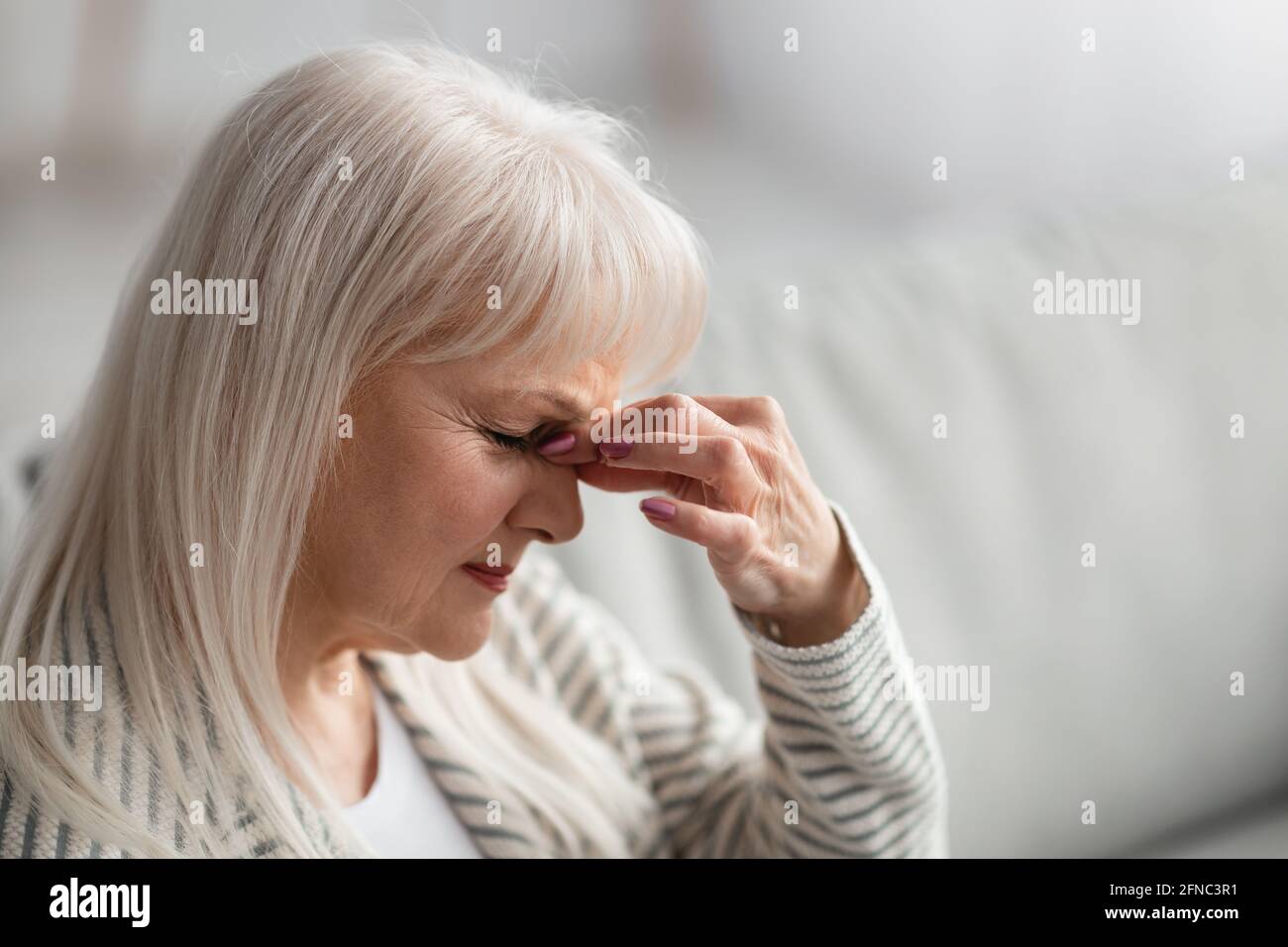 Fatiguée bouleversée femme âgée massant pont de nez Banque D'Images