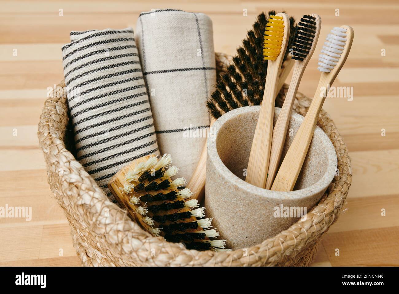 Ensemble de brosses à dents, serviettes roulées et deux brosses dans un petit panier sur parquet Banque D'Images