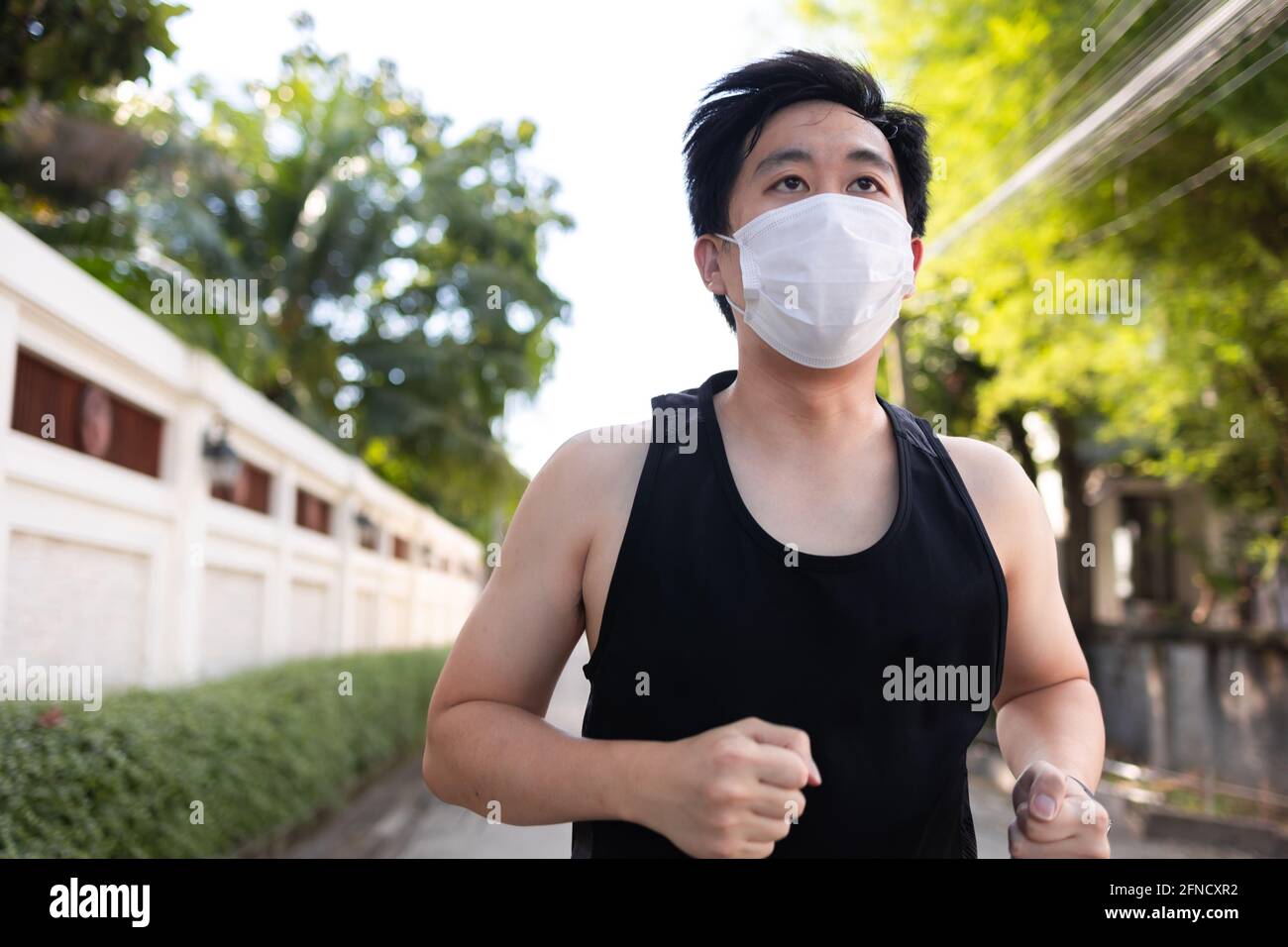 Jeune asiatique courant avec un masque facial dans la ville. Un coureur de sexe masculin fait de l'exercice et du jogging dans la rue Banque D'Images