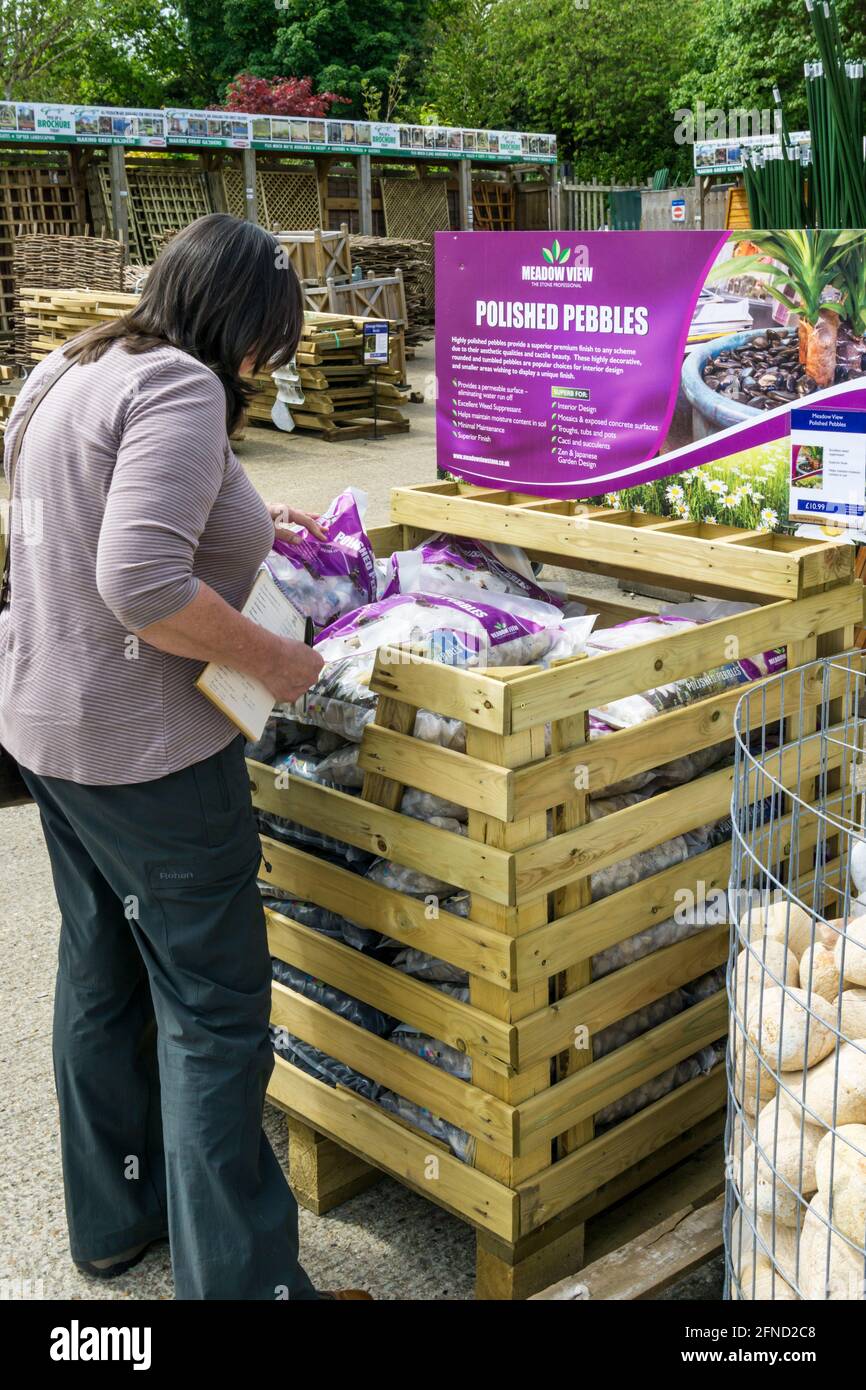 Une femme regardant des sacs de galets polis décoratifs à vendre dans un centre de jardin. Banque D'Images