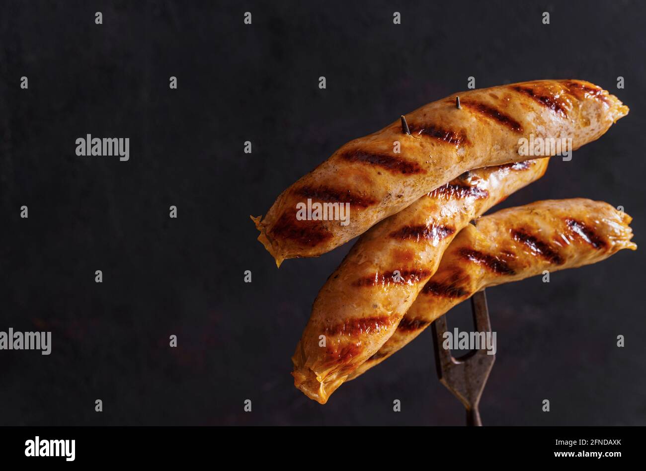 Trois saucisses grillées sur la fourchette en forme de lettre Z sur fond sombre avec espace de copie, faible mise au point peu profonde Banque D'Images