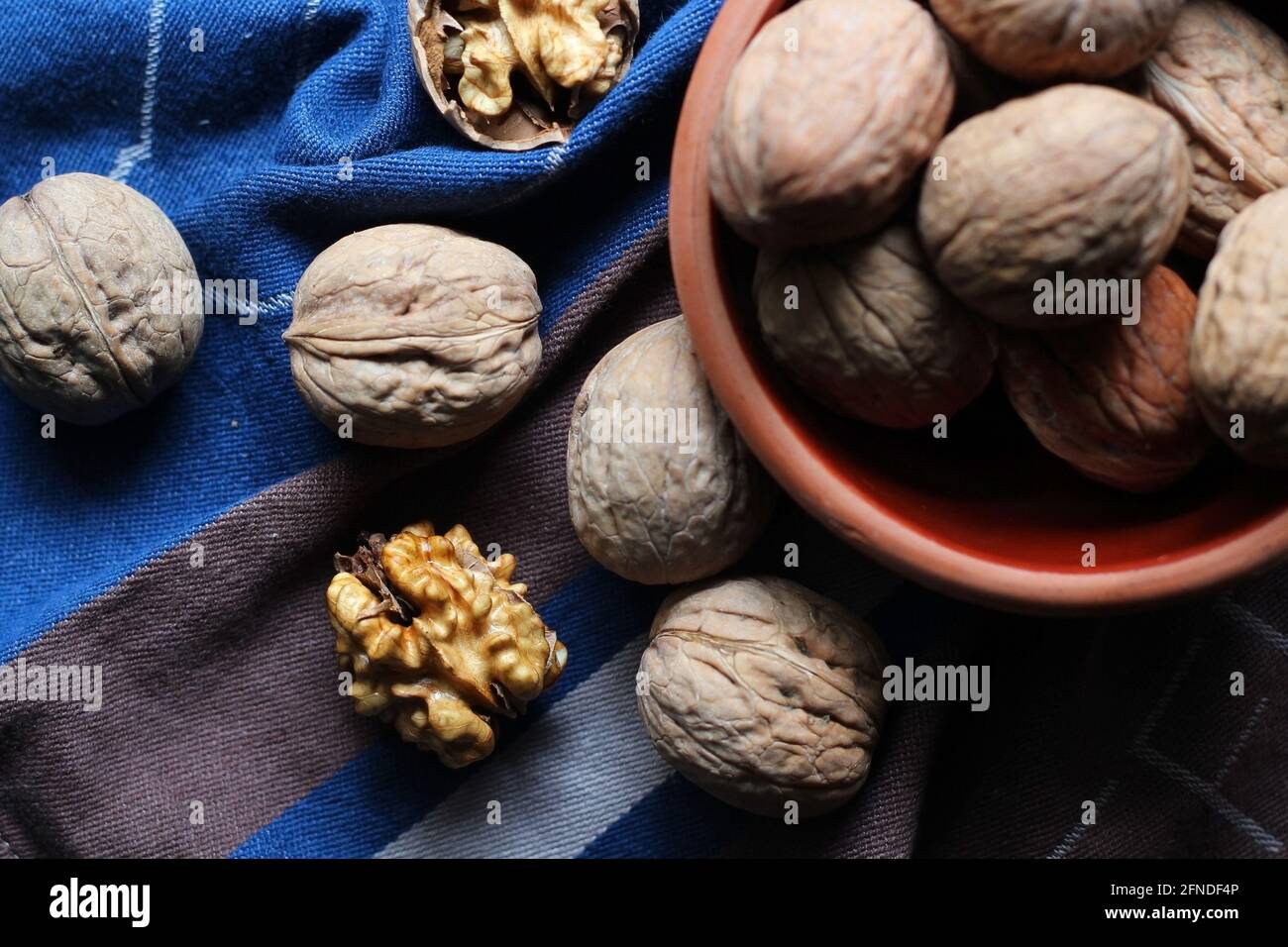 Des noix décortiquées et fissurées dispersées du bol sur un chiffon de cuisine en coton bleu et brun ont été photographiées en mode sombre. Concept créatif. Banque D'Images