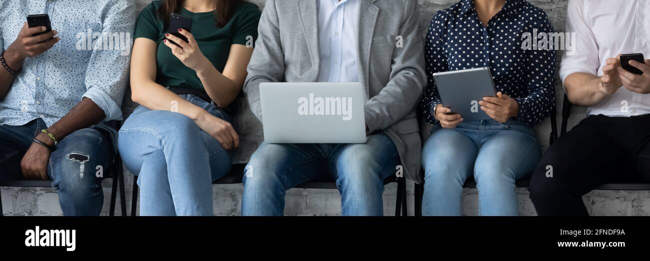 Groupe diversifié de clients assis dans la file, tenant des gadgets numériques Banque D'Images