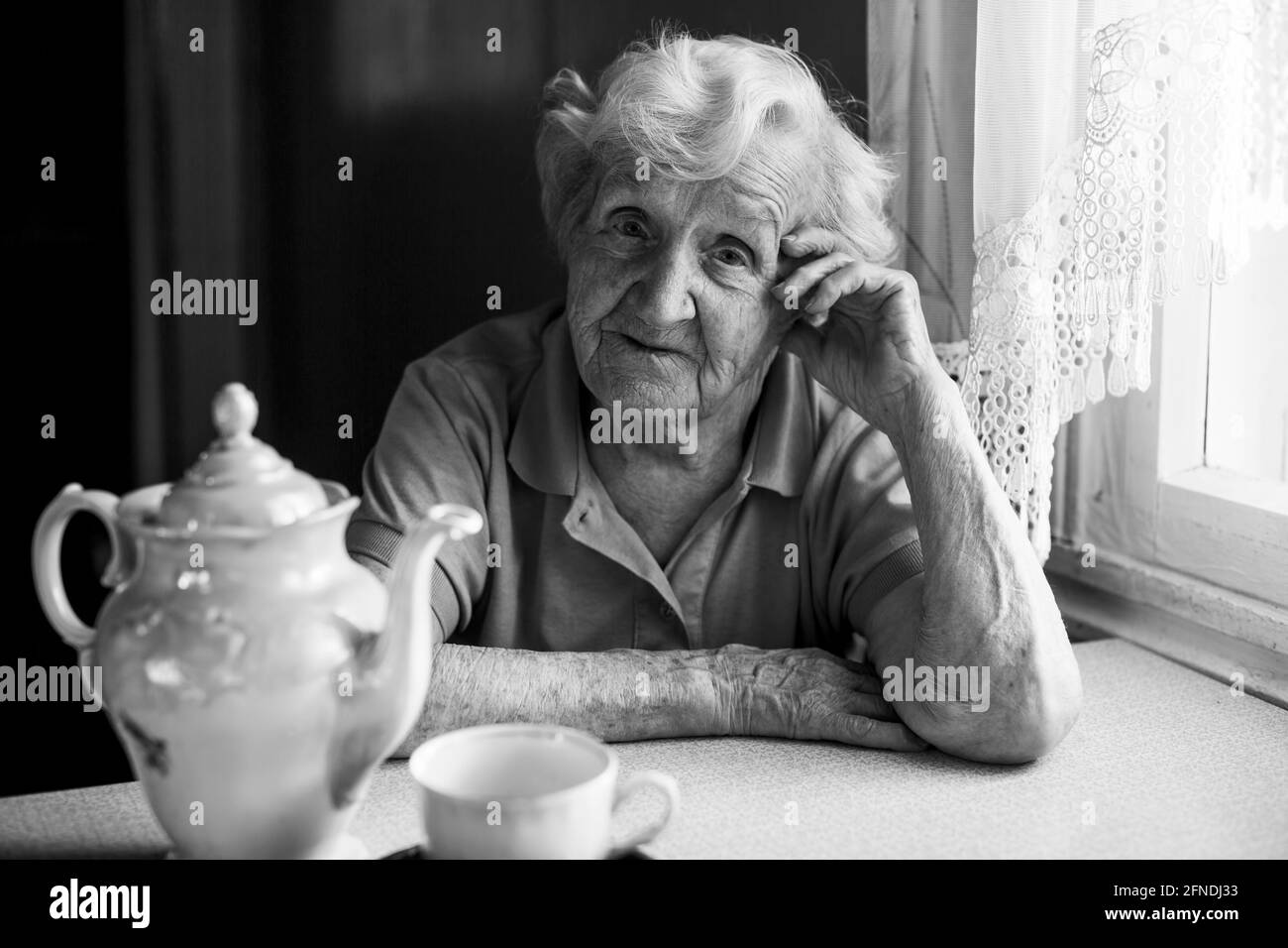 Portrait d'une vieille femme assise à la table avec une tasse de thé. Banque D'Images