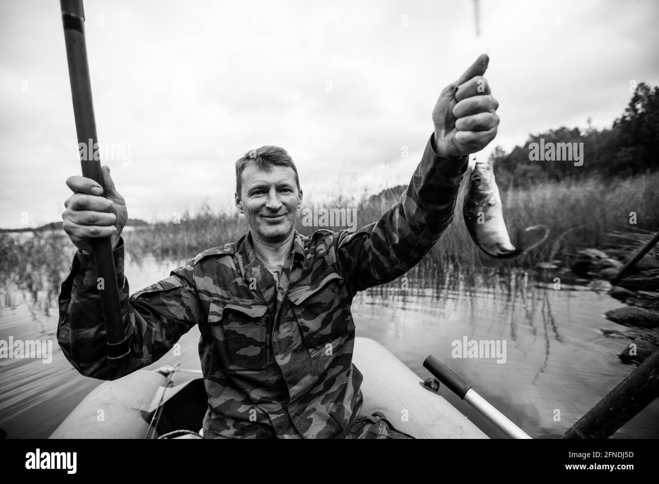 Un pêcheur de canne à pêche sur la rivière sur un bateau en caoutchouc. Photo en noir et blanc. Banque D'Images