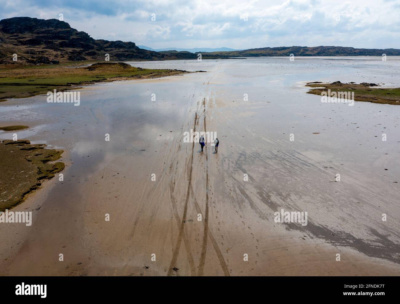 Deux marcheurs suivent des traces de pneus dans le sable menant à l'île marémotrice d'Oronsay, l'île Strand de Colonsay, en Écosse, au Royaume-Uni Banque D'Images