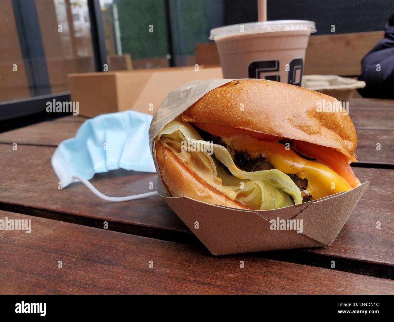Gros plan d'un cheeseburger placé sur une table avec une boisson derrière elle et un masque chirurgical sur le côté au restaurant Gott's Roadside à Walnut Creek, Californie, le 27 janvier 2021. () Banque D'Images