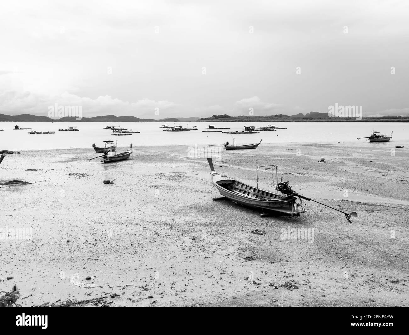 Bateau de pêche à longue queue en bois de villageois vides dans la boue de plage près de la mer avec des bateaux flottants près de l'île dans le style noir et blanc. Pêcheur thaïlandais Banque D'Images