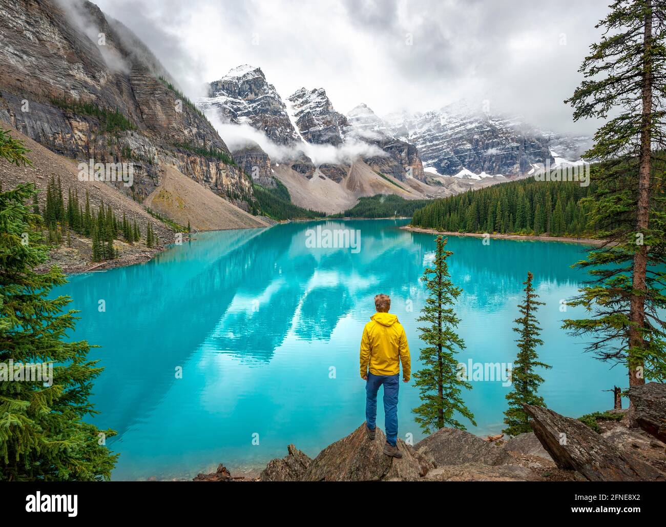 Jeune homme regardant les montagnes, pics de montagne nuageux, reflet dans le lac glaciaire turquoise, lac Moraine, vallée des dix pics, montagnes Rocheuses Banque D'Images