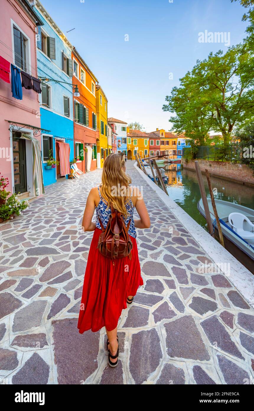 Jeune femme en face de maisons colorées, canal avec bateaux et façades de maisons colorées, île de Burano, Venise, Vénétie, Italie Banque D'Images