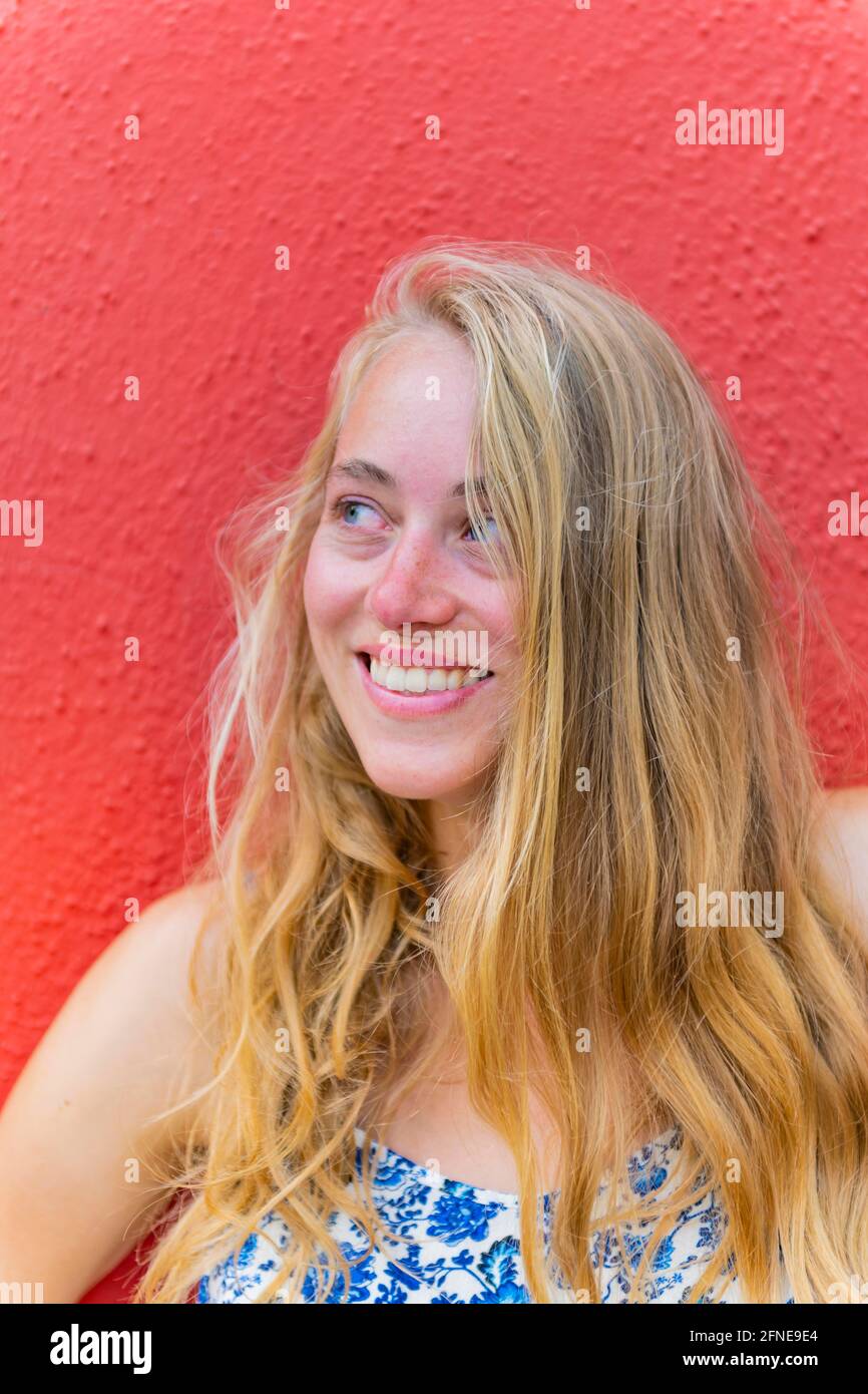 Portrait d'une jeune femme aux longs cheveux blond devant un mur rouge, riant, île de Burano, Venise, Vénétie, Italie Banque D'Images